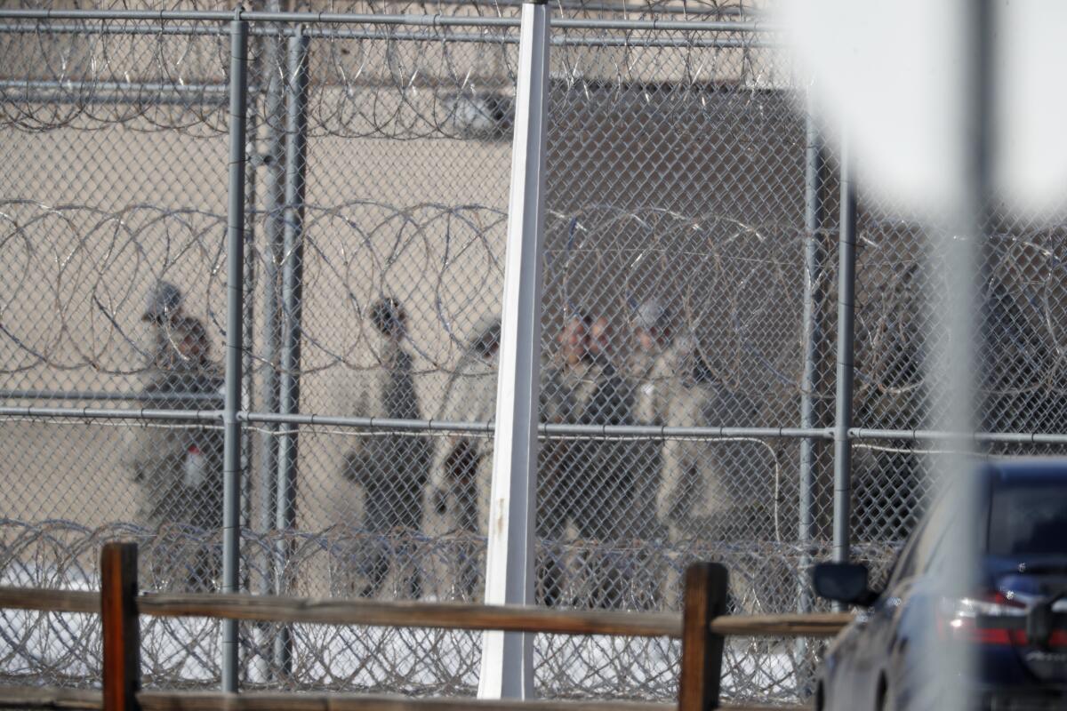 People on the other side of chain-link fencing with barbed wire at a federal prison.