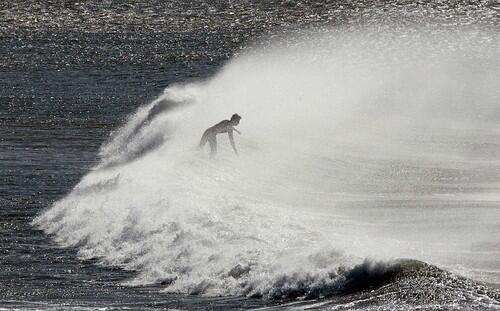 A surfer braves the cold, dry wind to catch a late-autumn wave at Huntington Beach.