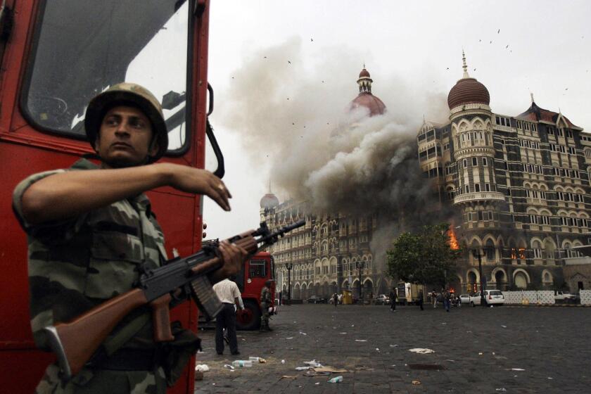 In this Nov. 29, 2008, file photo, an Indian soldier takes cover as the Taj Mahal hotel burns during gun battle between Indian military and militants inside the hotel in Mumbai, India. A Pakistani-American who helped plan a 2008 attack has told a court in India that he traveled to India seven times to scout potential targets for a Pakistan-based group.