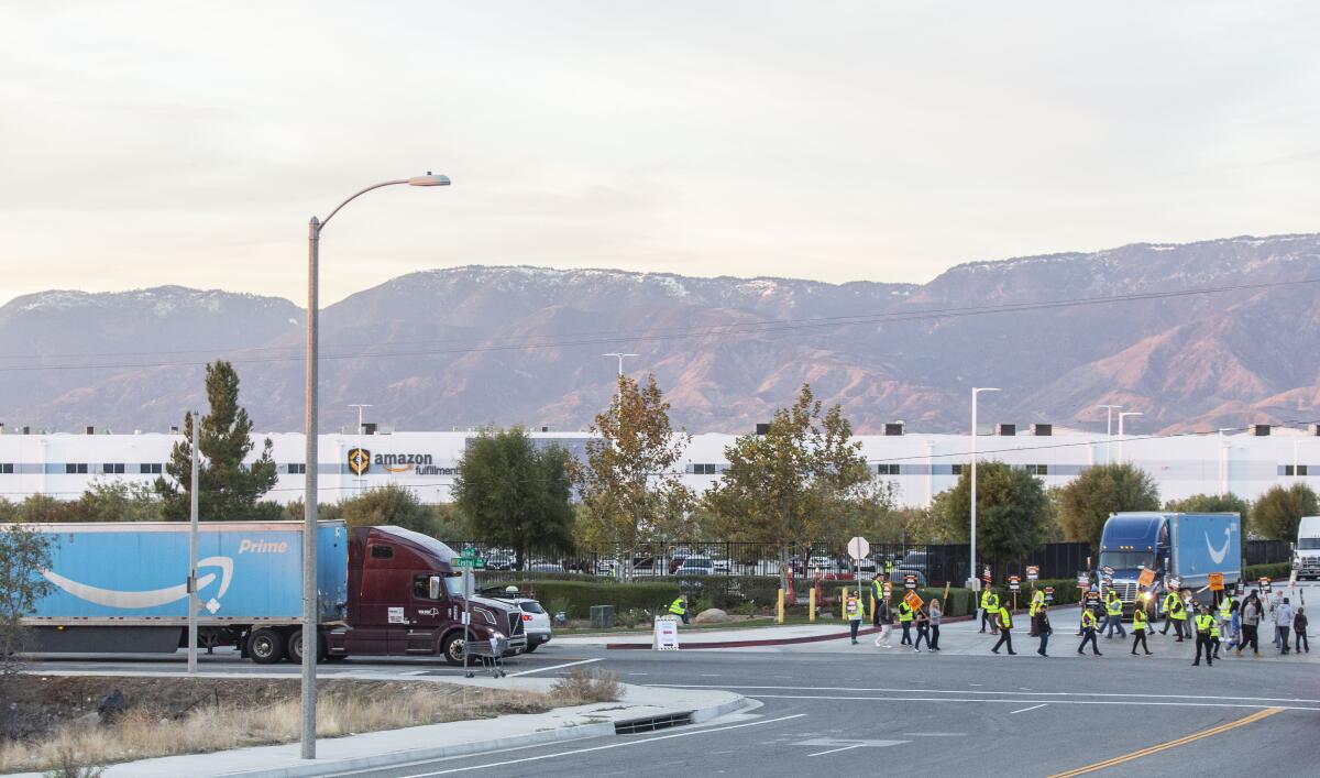 An Amazon Prime truck and a circle of people carrying picket signs in front of a large Amazon warehouse