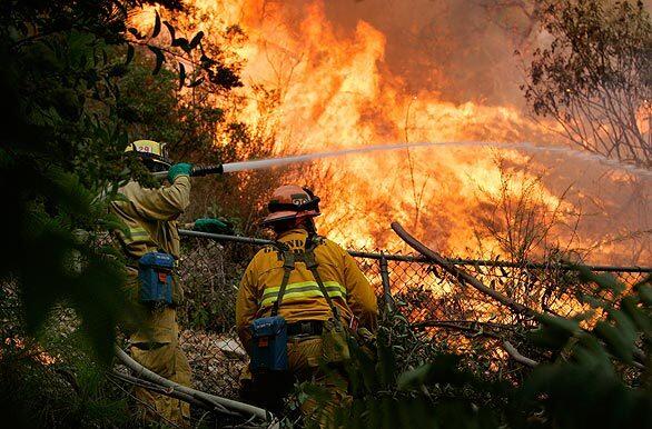 Firefighters douse brush as flames burn in a canyon, moving away from a home on Arnell Place in La Crescenta on Tuesday.
