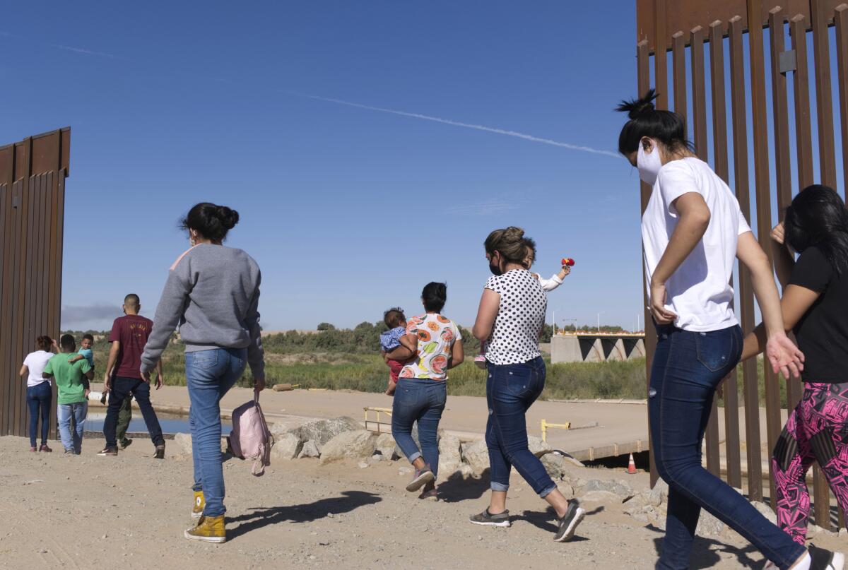 FILE - A group of Brazilian migrants make their way around a gap in the U.S.-Mexico border in Yuma, Ariz., seeking asylum in the U.S. after crossing over from Mexico, June 8, 2021. Two Republican border-state governors who are investing billions of dollars on immigration enforcement and hours at the podium blasting the Biden administration policies have found two unlikely allies: Democratic mayors Muriel Bowser of Washington, D.C., and Eric Adams of New York. The mayors' recent overtures for federal aid is a response to Texas and Arizona busing migrants away from the border, a months-old practice that has been long on political theater and short on practical impact. (AP Photo/Eugene Garcia, File)