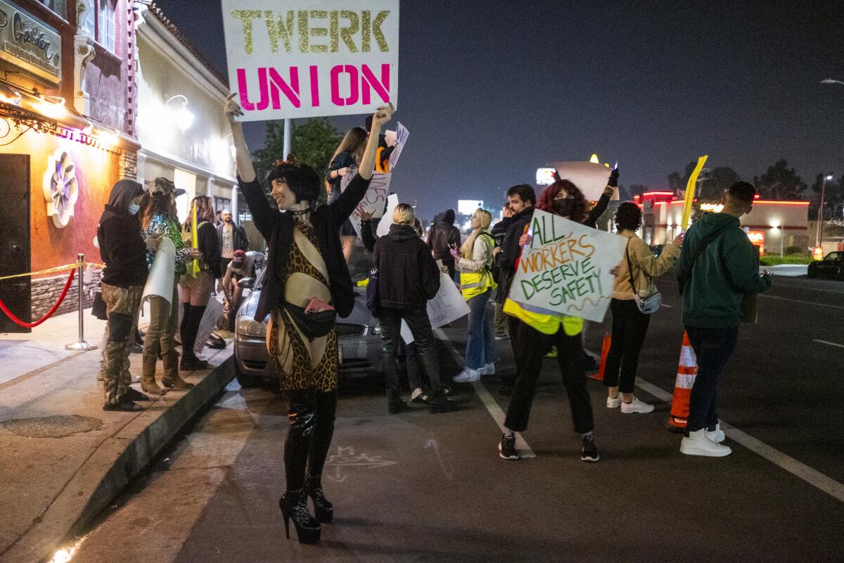 A woman holds up sign that says "Twerk Union" in front of a strip club.