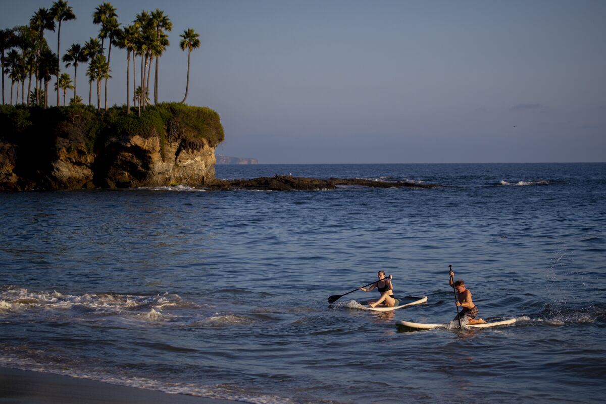 Paddleboarders take a scenic sunset cruise amid warm weather in Crescent Bay Beach in Laguna Beach.