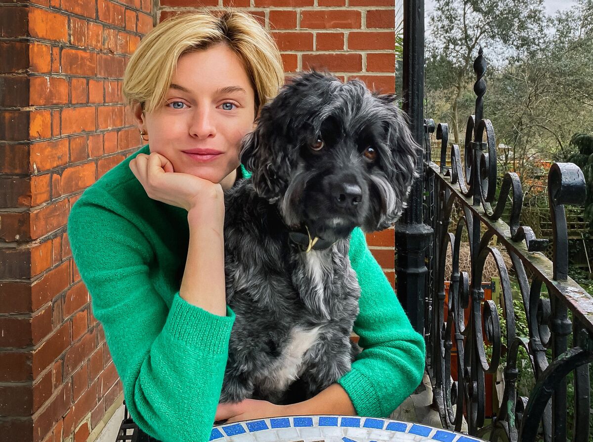 Emma Corrin (“The Crown”) sits on a balcony holding her dog.
