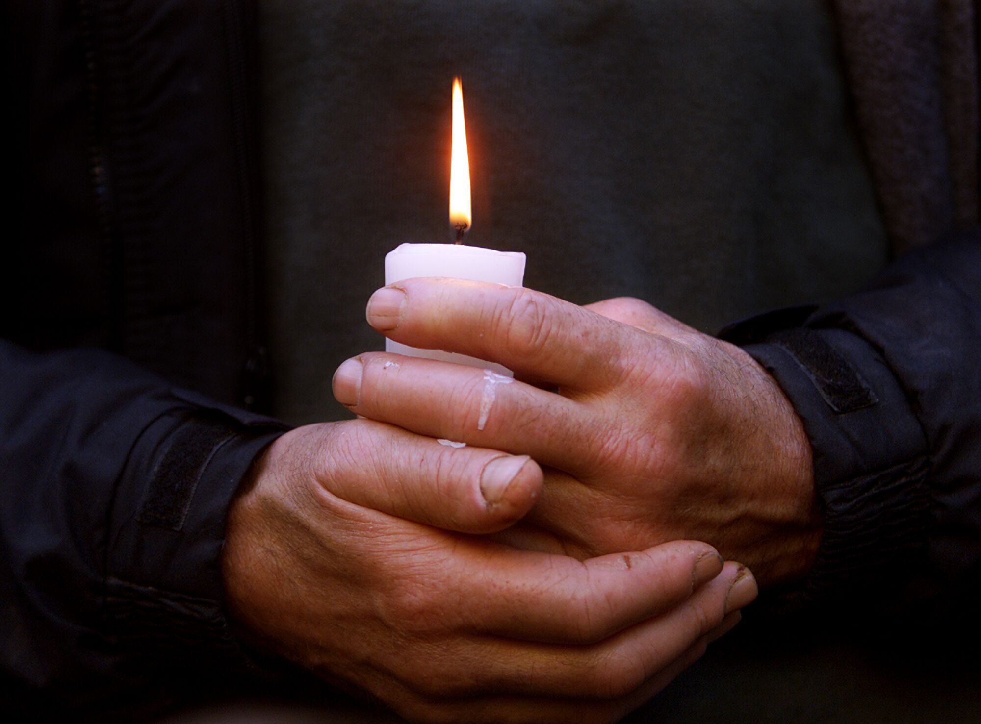 A pair of hands hold a lit candle