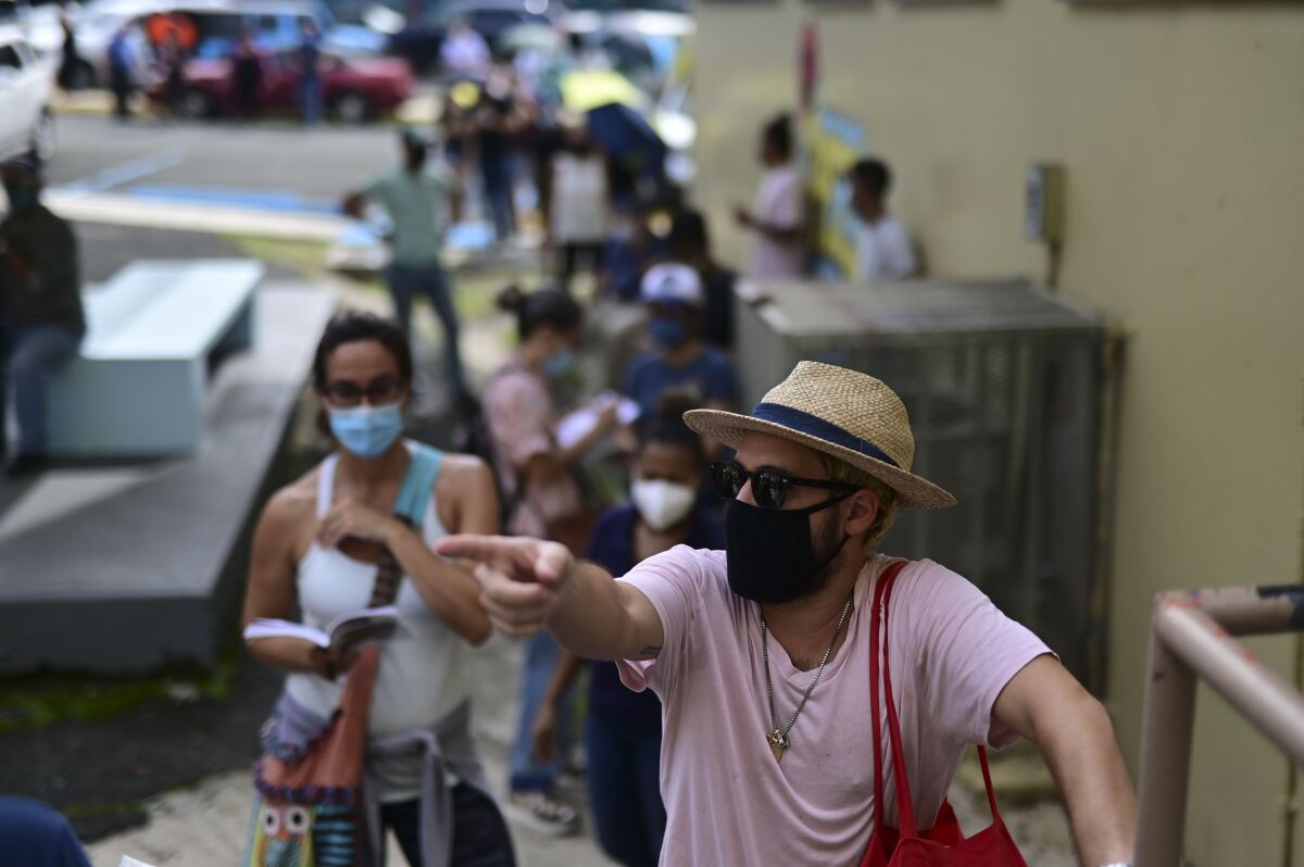 People wearing masks amid the COVID-19 pandemic wait in line to vote in the general election at a polling center set up at the Rafael Labra School in San Juan, Puerto Rico, Tuesday, Nov. 3, 2020. In addition to electing a governor, Puerto Ricans are voting in a non-binding referendum on statehood. (AP Photo/Carlos Giusti)