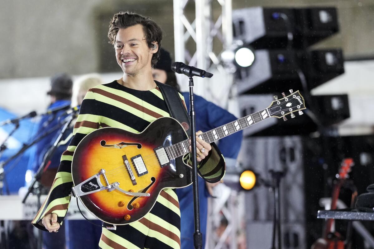 A man wearing a striped bodysuit, holding a guitar and standing in front of a microphone onstage.