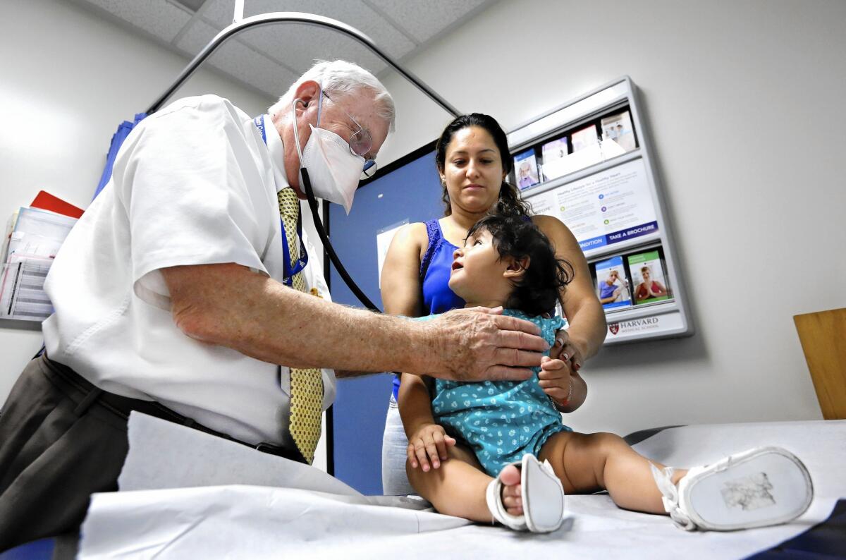Dr. Dennis Mull, 77, examines Emily Jimenez, 8 months, at South Central Family Health Center in Los Angeles. Holdling Emily is her mother, Waldina Baltista. Mull is an old-fashioned physician who uses note cards instead of computers.