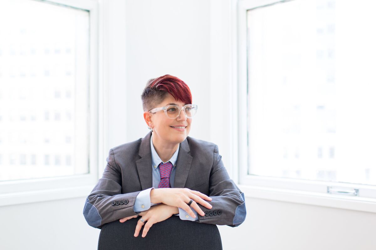 Annalee Newitz, in a suit jacket with elbow patches and a tie, sits backward on a chair.