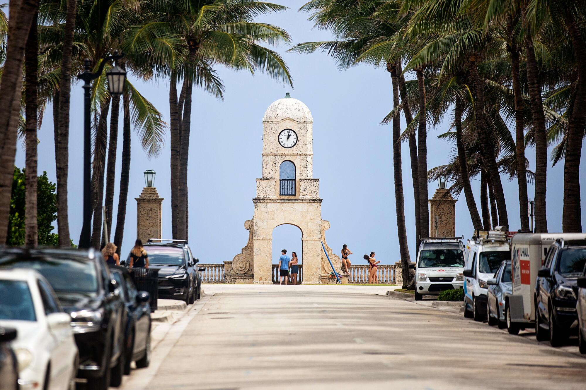 A large clock tower at the end of a palm-tree-lined street