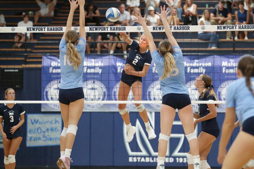 Emma Olson of Newport Harbor (2) finds a gap for a kill between Molly Machoskie (10) and Savi Dennis, during Battle of the Bay girls volleyball match against Corona Del Mar on Tuesday.