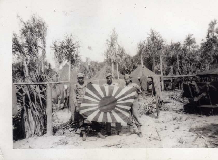 El soldado de primera clase Ernest Racer, a la izquierda, está con otros soldados y una bandera japonesa capturada durante la Segunda Guerra Mundial.