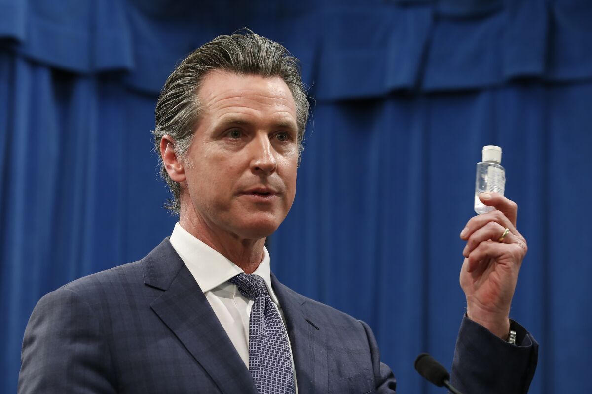 Governor Gavin Newsom holds up a bottle of hand sanitizer