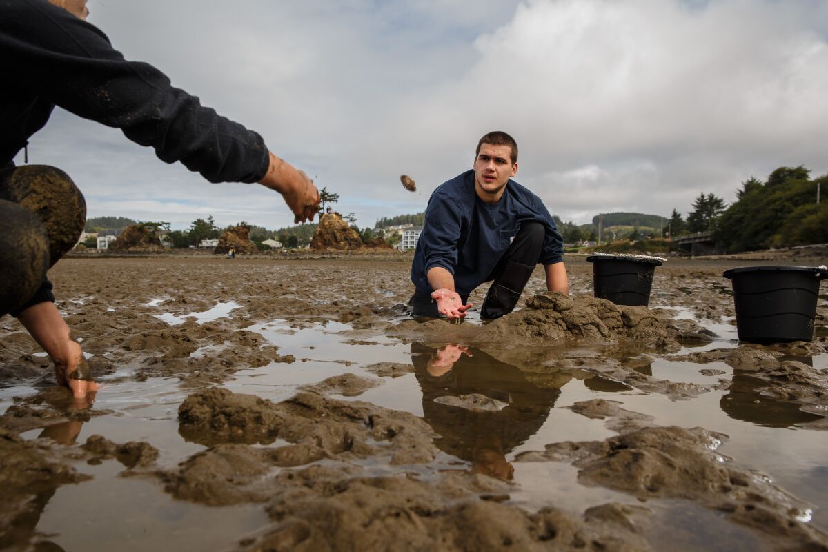 Olivia Michaels, 16, tosses a clam over to Conner Middleton, 16, as he digs for clams in Siletz Bay in Lincoln City, Ore. (Marcus Yam / Los Angeles Times)