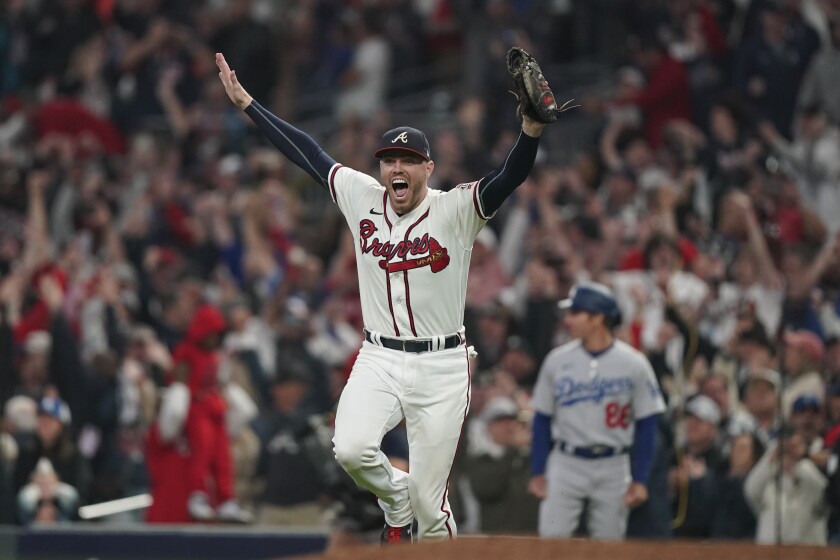 A man in a Braves uniform raises his hands and smiles on the field while fans are in the stands in the background
