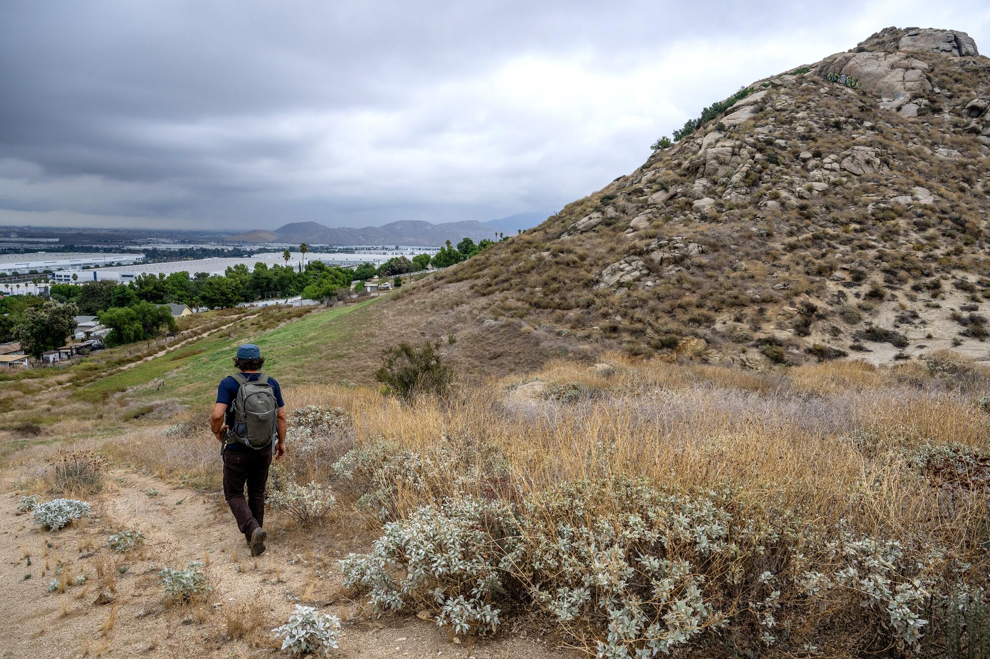 A man walks along a dirt path beside a hill.
