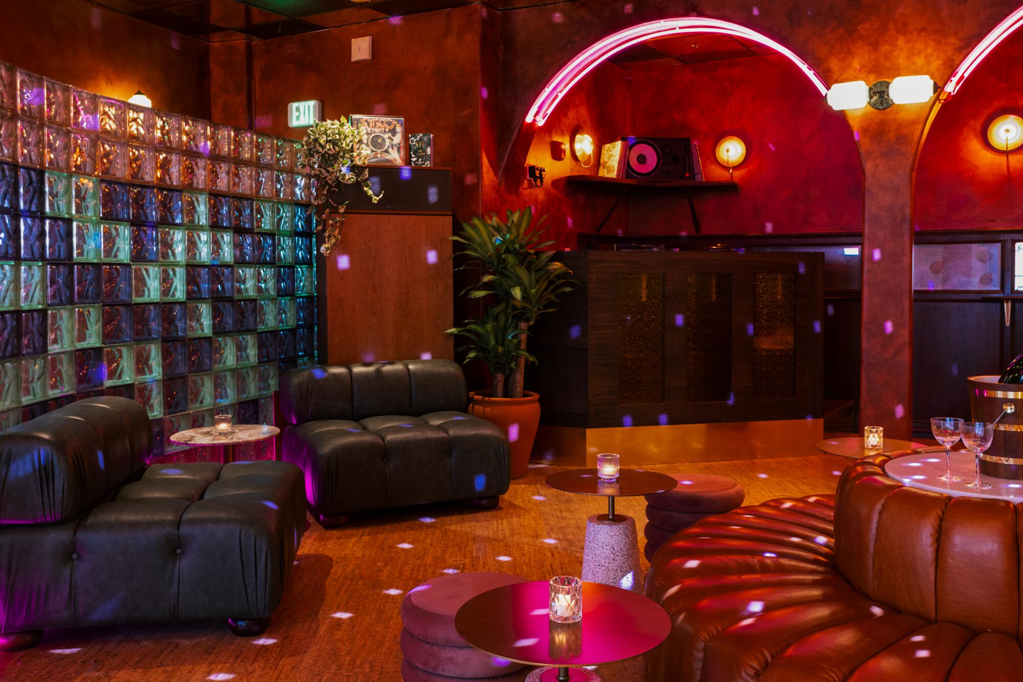 A dark bar interior with leather seating, pink neon over its archways and a glass block wall at one end.