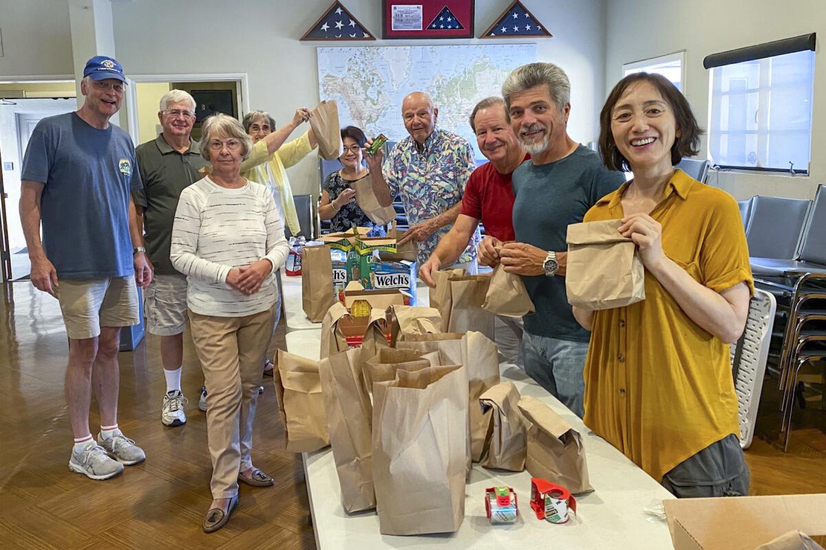 Volunteers with Ascencia stand by a table filled with brown bag lunches they helped make