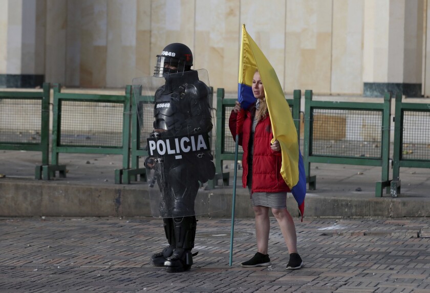 FILE - A woman holding a Colombian flag stands next to a police officer in riot gear during a protest in Bogota, Colombia, Monday, Sept. 21, 2020. Colombian police killed at least 10 people during protests that broke out in September of last year, following the death of a taxi driver who was beaten to death while in police custody, a report published Monday, Dec. 13, 2021, backed by the United Nations found. (AP Photo/Fernando Vergara, File)