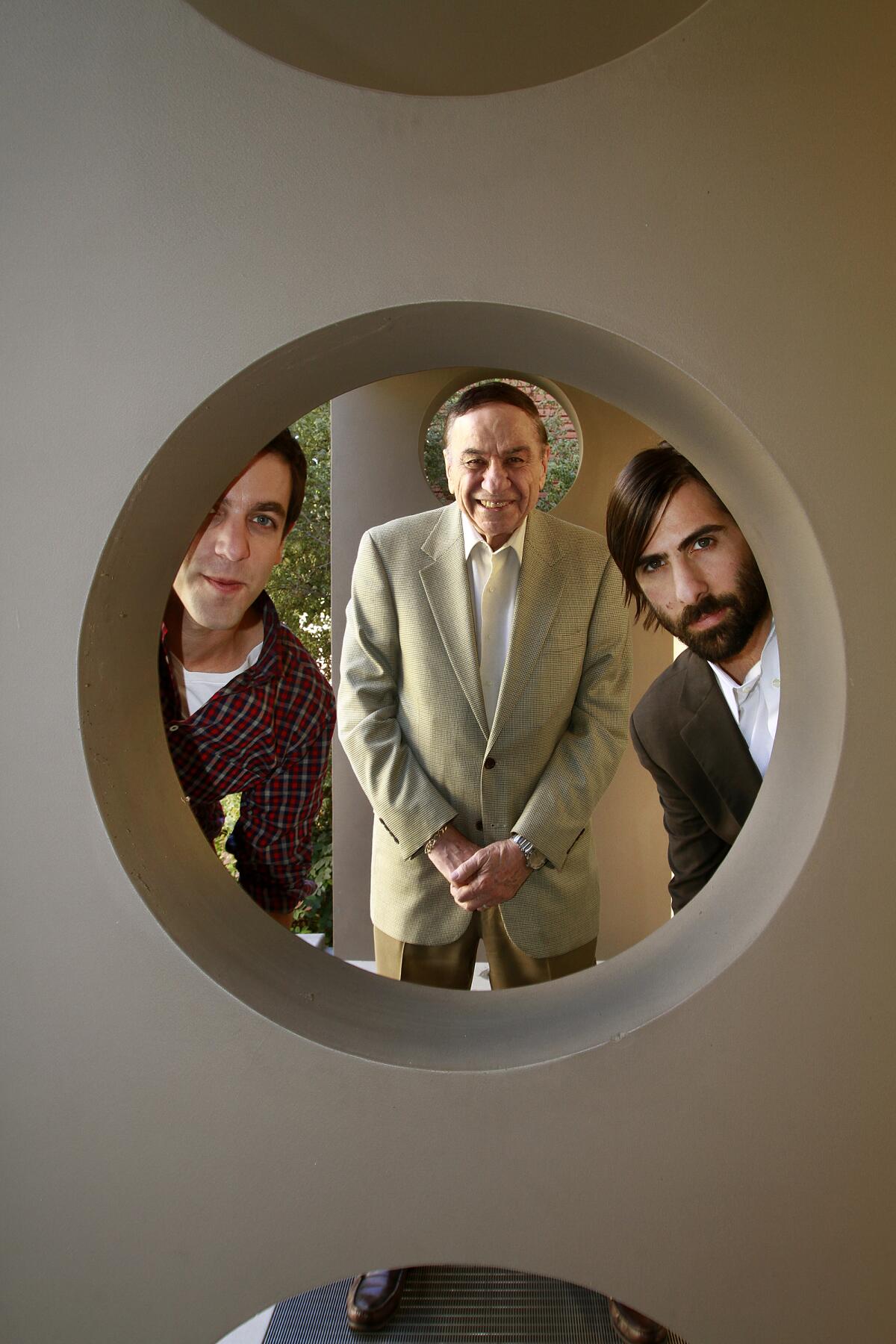 Three men peer through a circular opening in a wall