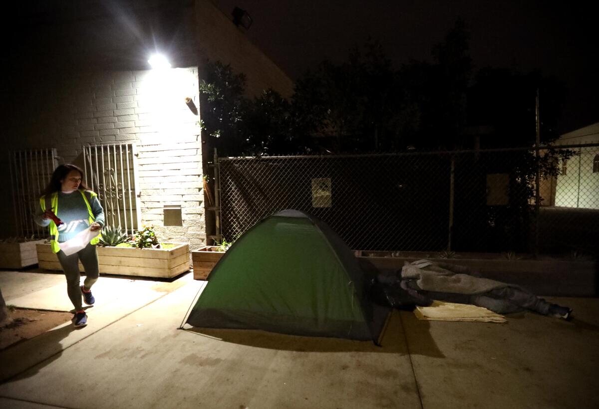 A man in a reflective safety vest approaches a tent at night.