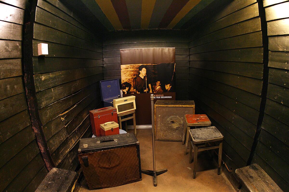 A wooden stage set with amplifiers and a microphone stand and a photo of Paul McCartney.