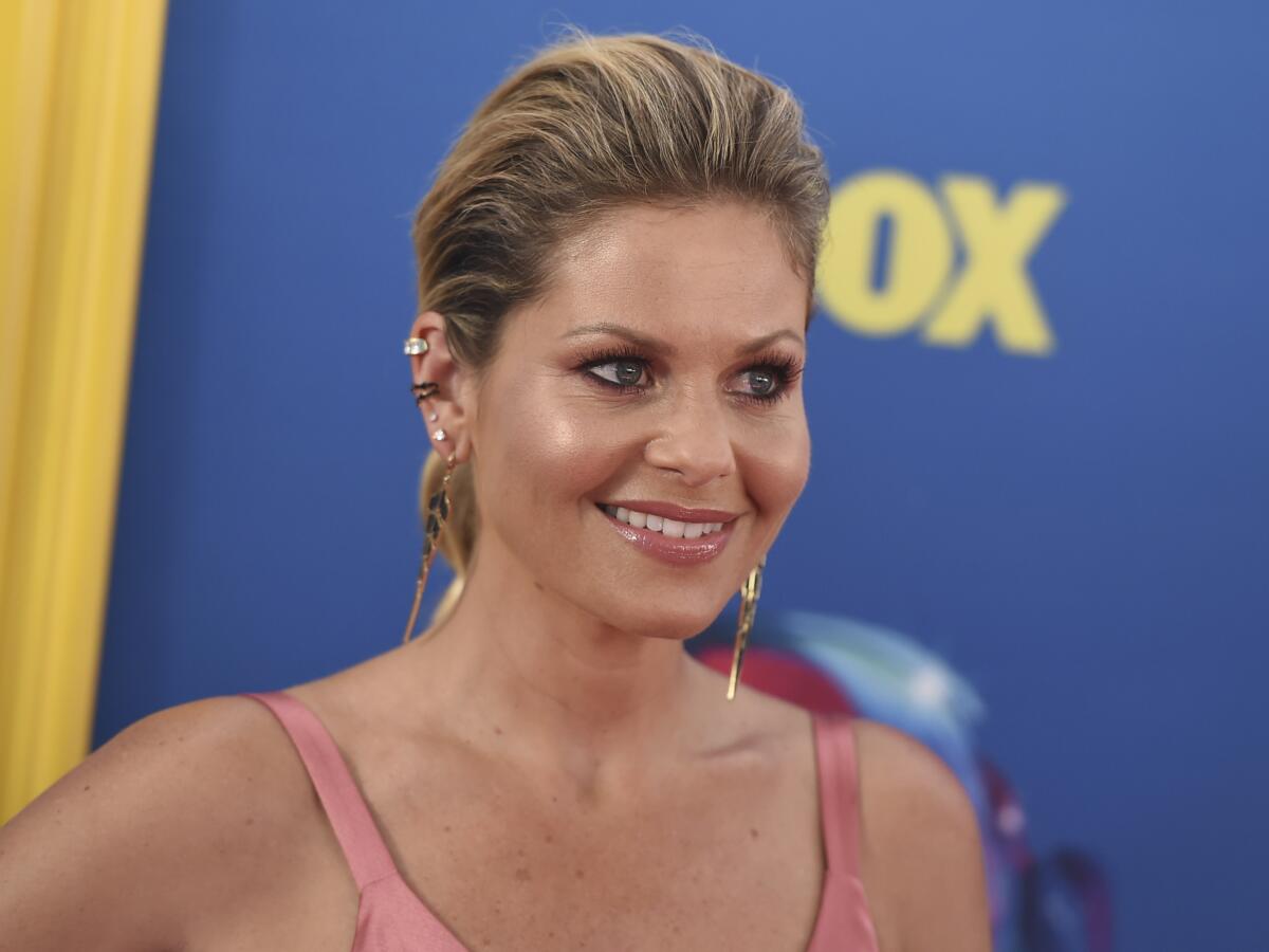 Candace Cameron Bure with her hair slicked back wearing a pink dress and gold dangling earrings