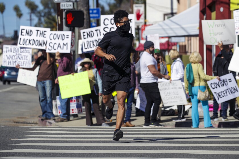 Thomas Miller jogs by protesters rallying against the COVID-19 vaccine and public health lockdowns near Dodger Stadium.