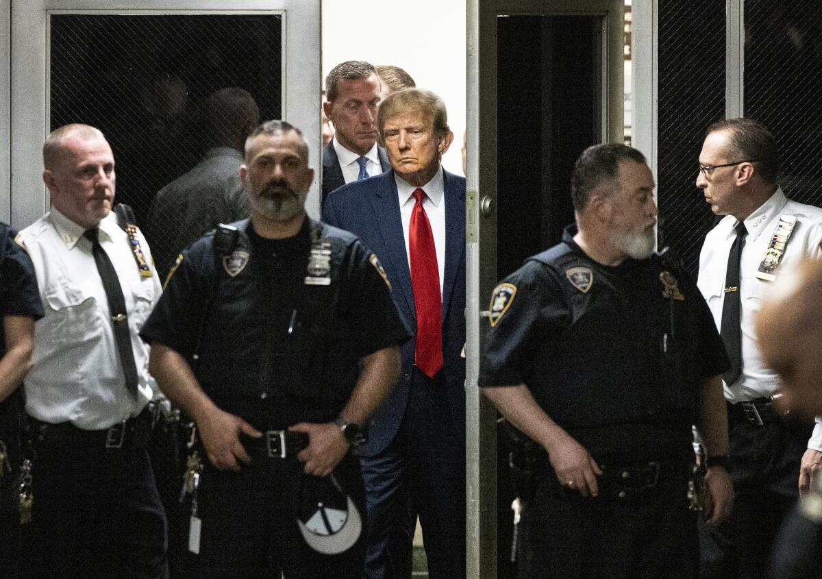 Donald Trump, surrounded by men in ties and uniforms, walks through a doorway 