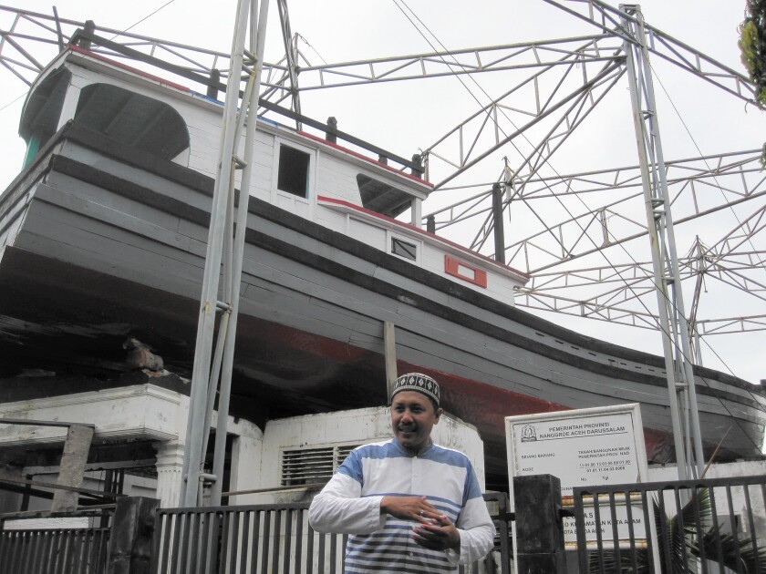 Mujiburrizal, 37, stands in front of the 75-foot fishing boat that enabled him to survive the tsunami. The boat was carried by waves and landed on top of a two-story house next door. After the waters receded, officials secured the boat to the house and turned it into a sort of museum exhibit.