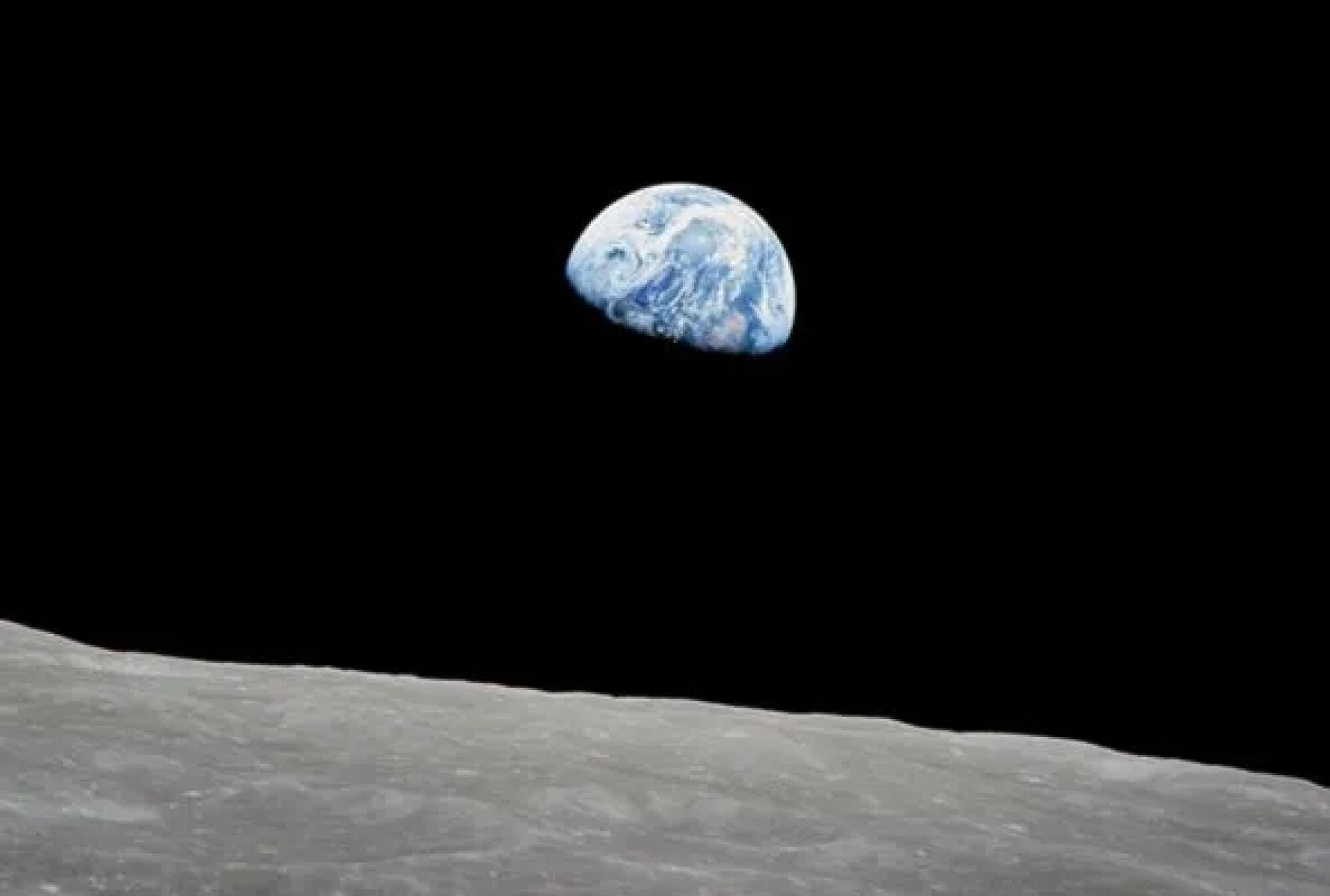 A gibbous Earth in a black sky over the gray surface of the moon