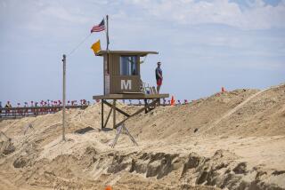 Brandon LaGrotta, a Newport Beach lifeguard, stands watch at a tower near the Balboa Pier on Wednesday, June 23. The city of Newport Beach recently built a sand berm to protect coastal properties from high tides.