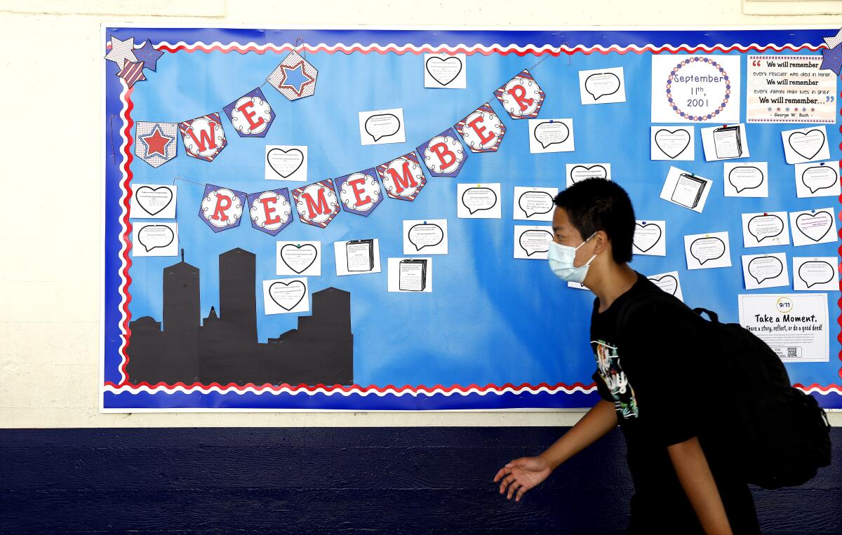 A masked student walks past a bulletin board at a school.