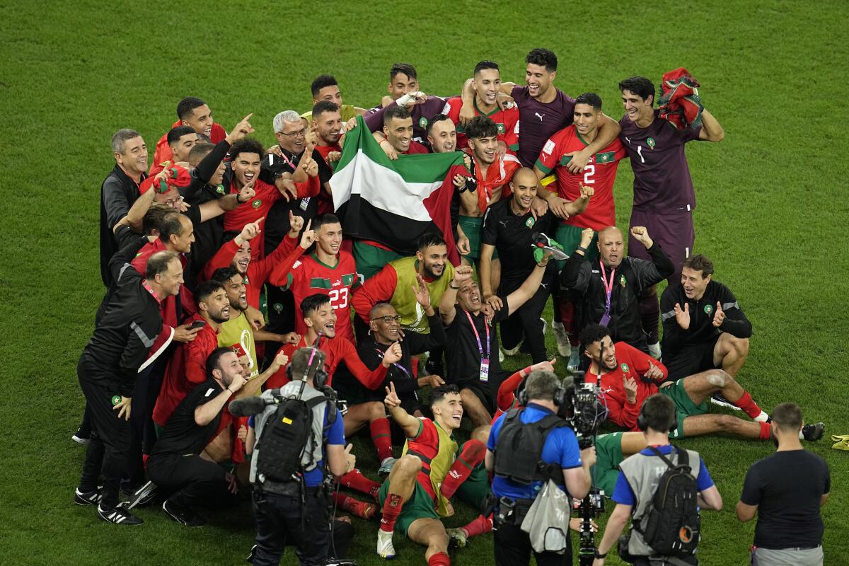 A group of smiling people hold a red-white-black-and-green flag on a soccer field
