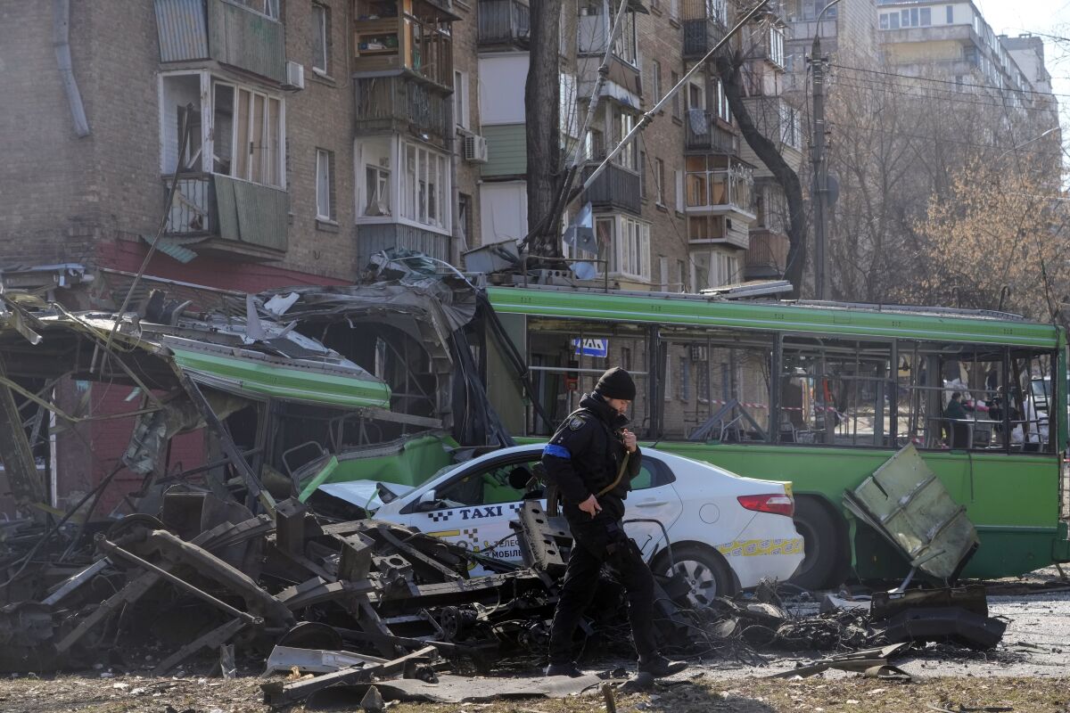 A Ukrainian soldier passes by a destroyed a trolleybus and taxi after a Russian bombing attack in Kyiv, Ukraine, Monday, March 14, 2022. (AP Photo/Efrem Lukatsky)