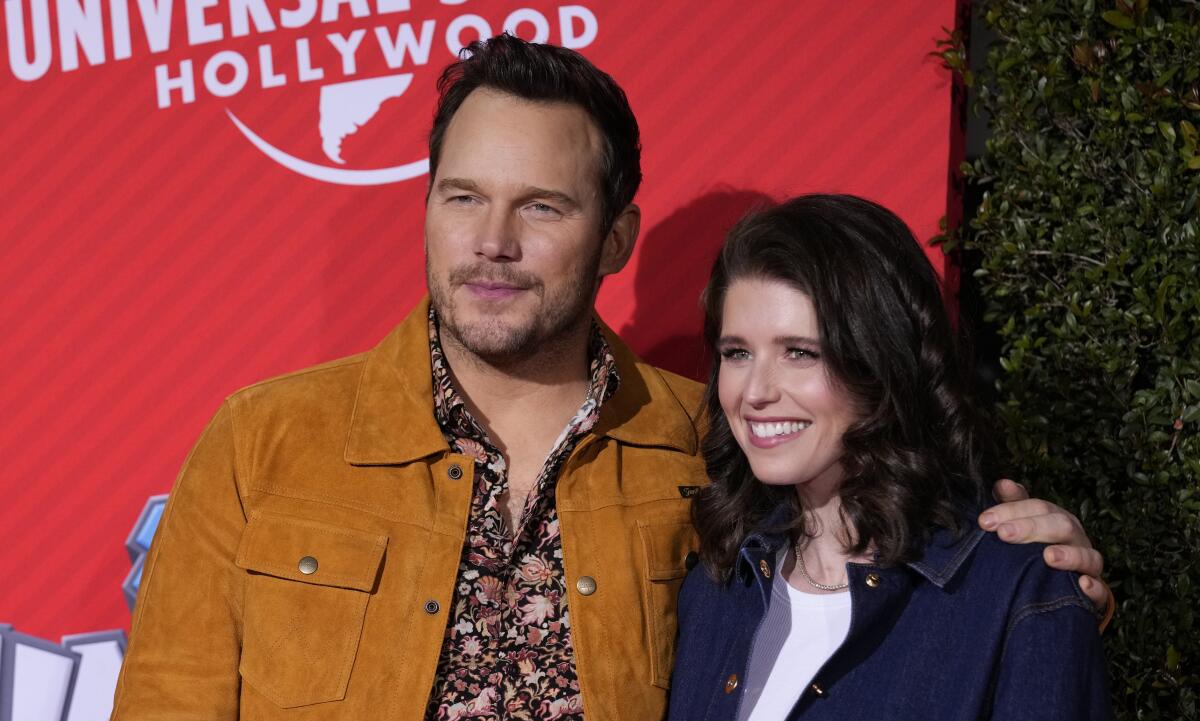 Chris Pratt in a brown jacket and floral-pattern shirt posing with Katherine Schwarzenegger in a dark jacket and white top