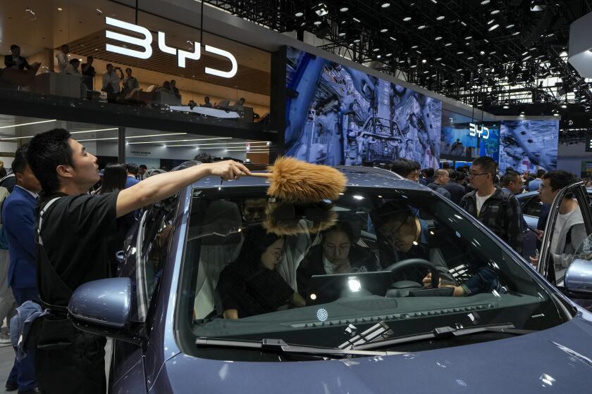 A worker wipes as visitors sit on a BYD Song Pro DM-i car model during the Auto China 2024 in Beijing, Sunday, April 28, 2024. Global automakers and EV startups unveiled new models and concept cars at China's largest auto show, with a focus on the nation's transformation into a major market and production base for digitally connected, new-energy vehicles. (AP Photo/Andy Wong)