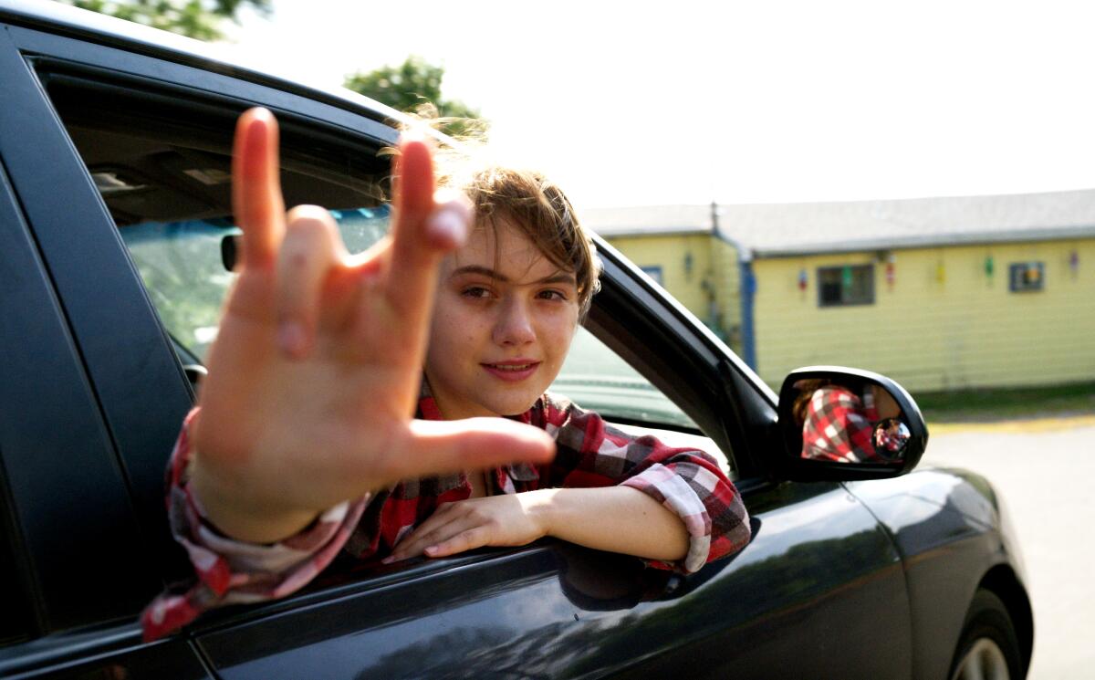 Emilia Jones leans out a car window and flashed an "I love you" hand sign in the film “CODA.” 