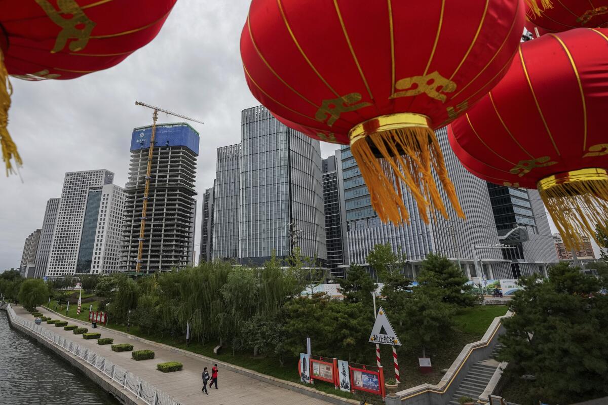 People walk along a riverbank near a commercial office buildings under construction in Tongzhou.