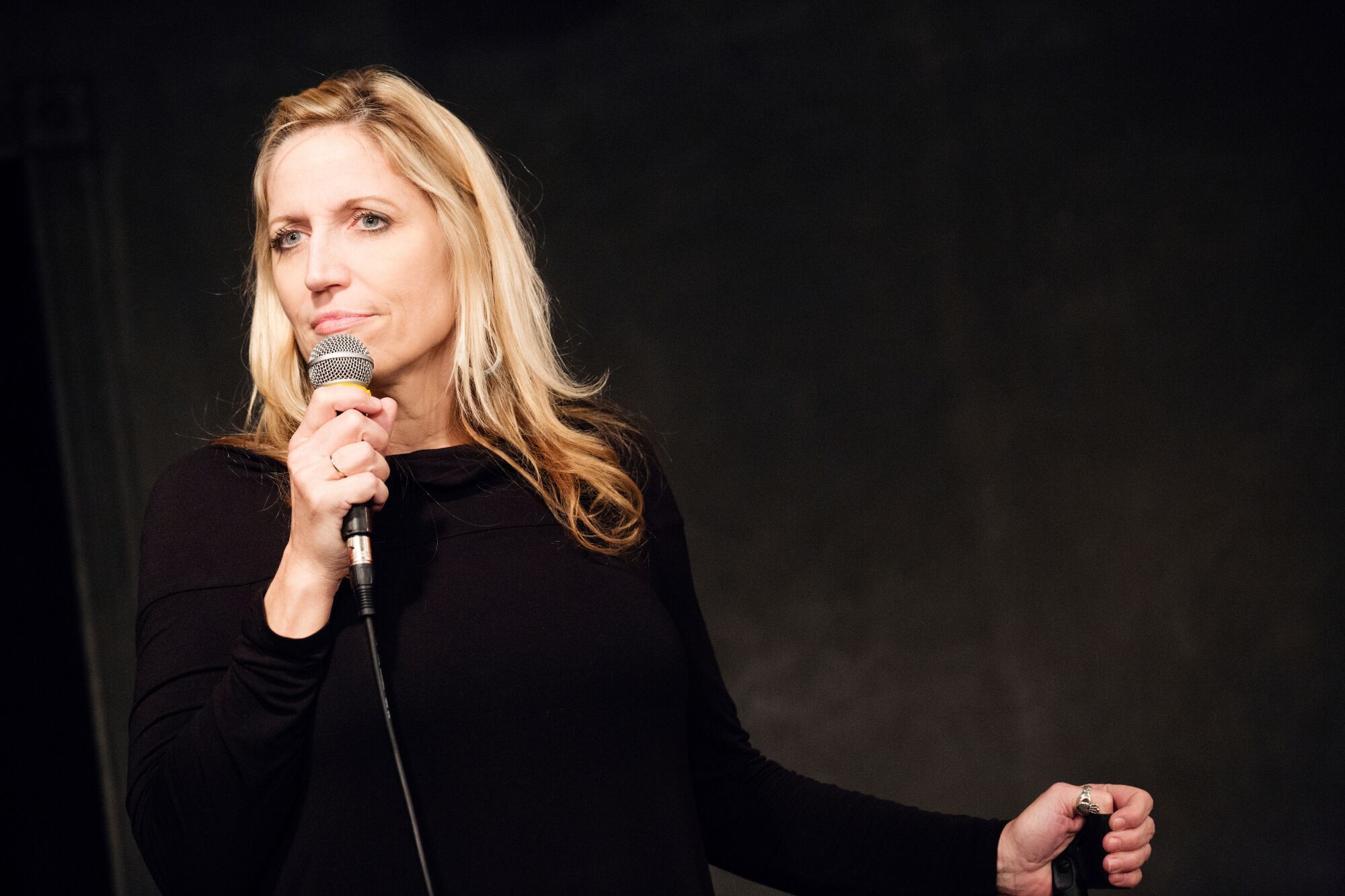 Comedian Laurie Kilmartin stands on stage with a microphone