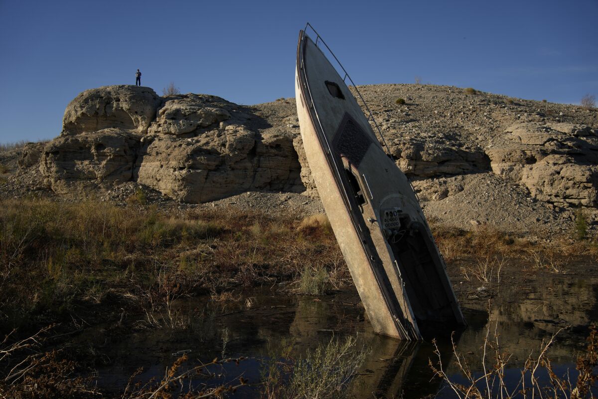 A man stands on a hill overlooking a formerly sunken boat standing upright into the air with its stern buried in the mud along the shoreline of Lake Mead at the Lake Mead National Recreation Area, Friday, Jan. 27, 2023, near Boulder City, Nev. Competing priorities, outsized demands and the federal government's retreat from a threatened deadline all combined to thwart a voluntary deal last summer on how to drastically cut water use from the parched Colorado River, according to emails obtained by The Associated Press. (AP Photo/John Locher)