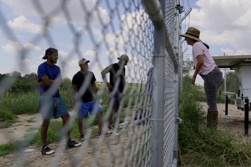 Magali Urbina, right, talks through her fence to migrants who crossed the Rio Grande illegally at her pecan farm, Heavenly Farms, Friday, Aug. 26, 2022, in Eagle Pass, Texas. The Texas National Guard and state troopers built a fence around Heavenly Farms and, in mid-August, locked a gate to arrest migrants after crossing the Rio Grande illegally. The U.S. Border Patrol felt the lock impeded operations and had it removed. (AP Photo/Eric Gay)