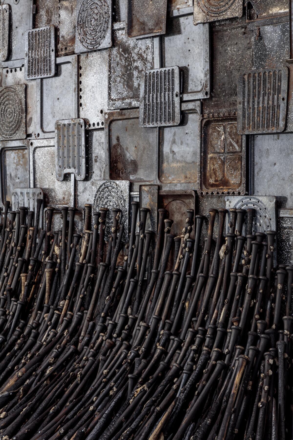 A vertical image shows dozens of burned baseball bats leaning against a wall covered in broiler pans.