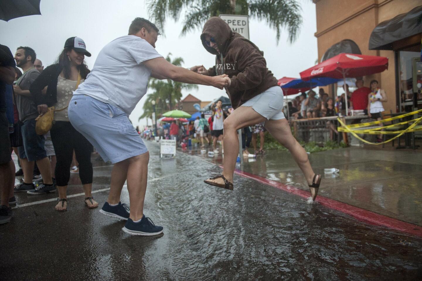 Jess Hoinacki helps Melisa Flores cross the gushing storm drains on University Avenue during the San Diego Pride Parade.