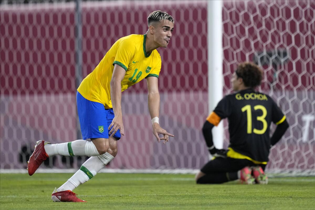 Brazil soccer player Reinier celebrates after scoring the winning goal as Mexico's Guillermo Ochoa kneels.