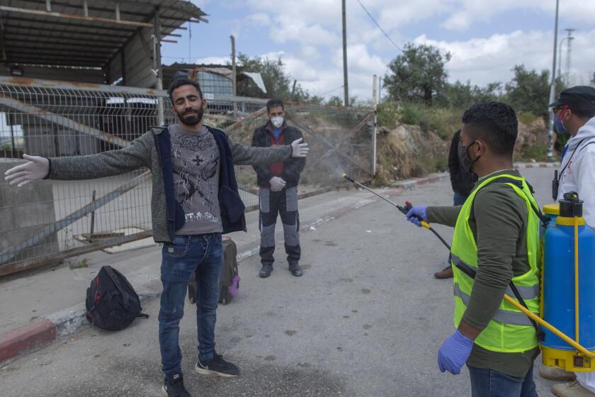 In this Tuesday, April 7, 2020 photo, a paramedic from the Palestinian Ministry of Health disinfects Palestinian laborers to help contain the coronavirus, as they exit an Israeli army checkpoint after returning from work in Israel, near the West Bank village of Nilin, west of Ramallah. The virus outbreak poses a major dilemma for tens of thousands of Palestinian laborers working inside Israel who can no longer freely travel back and forth. (AP Photo/Nasser Nasser)