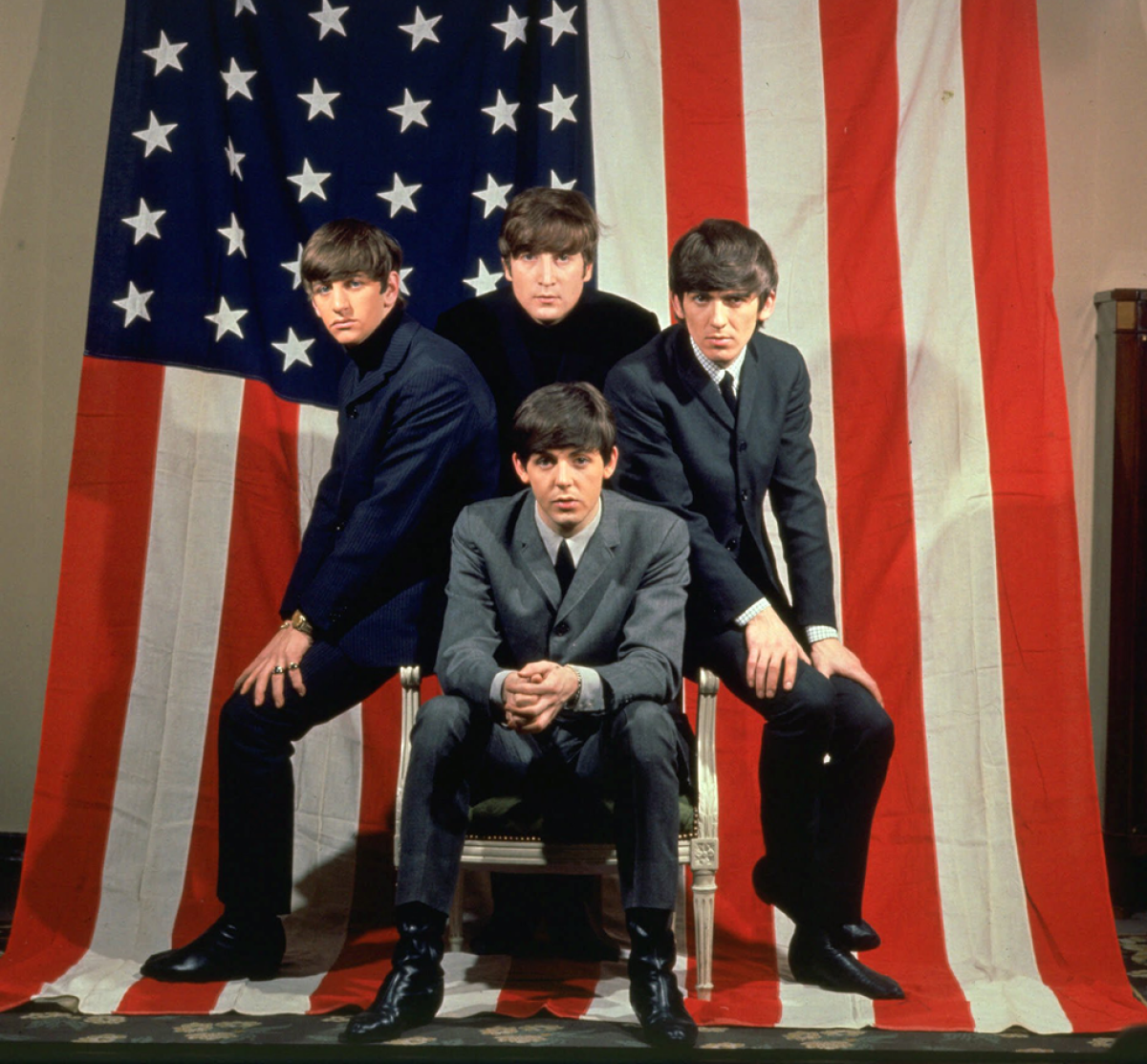 The Beatles, clockwise from top center, John Lennon, George Harrison, Paul McCartney and Ringo Starr, pose with an American flag in a Paris photo studio prior to their first visit to the United States in 1964.