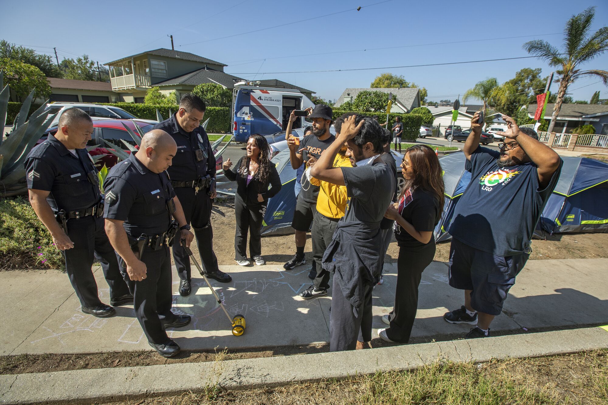 A police officer holds a measuring tool to mark a point on the sidewalk as protesters look on.