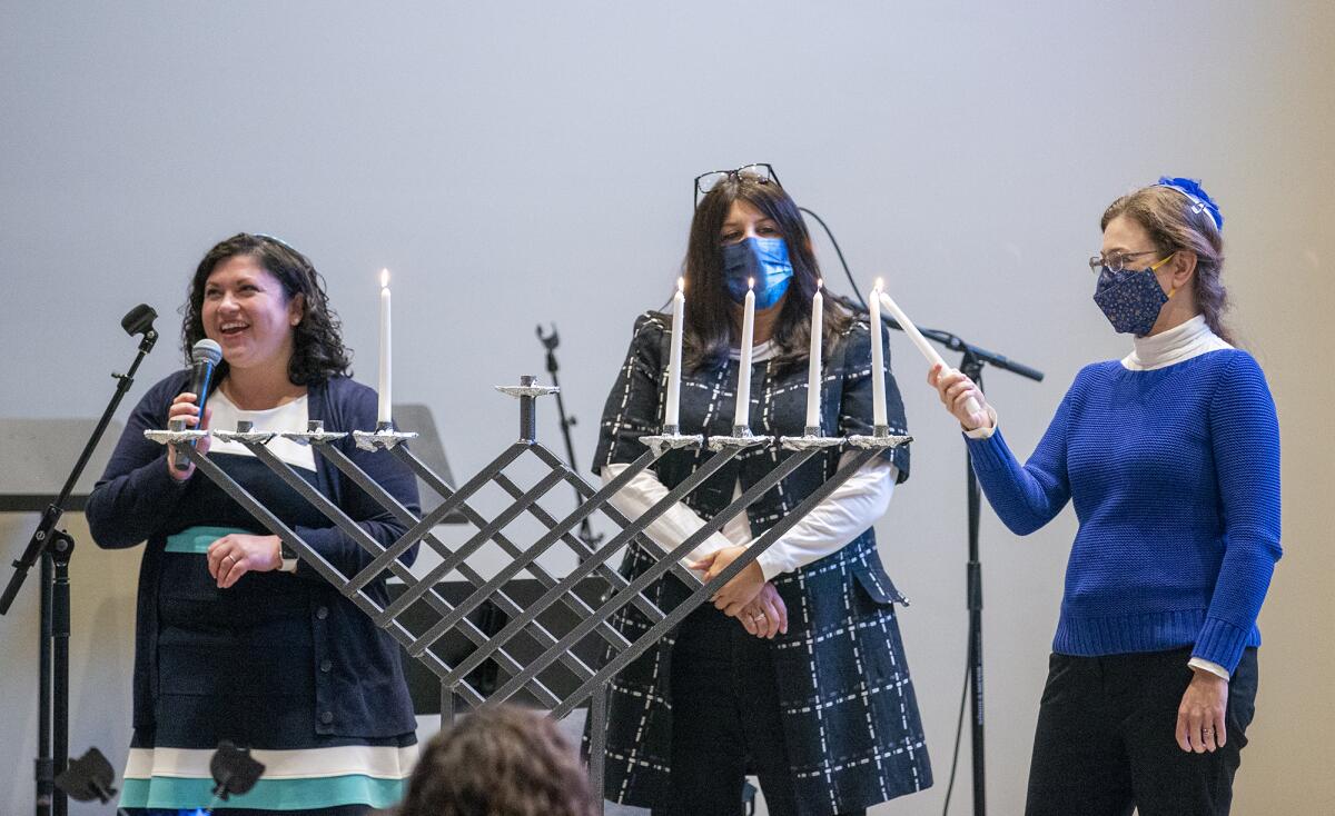 Rabbi Sarah DePaolo, left, Rabbi Corie Yutkin, center, and Rabbi Miriam Philips, right, light a menorah Thursday.